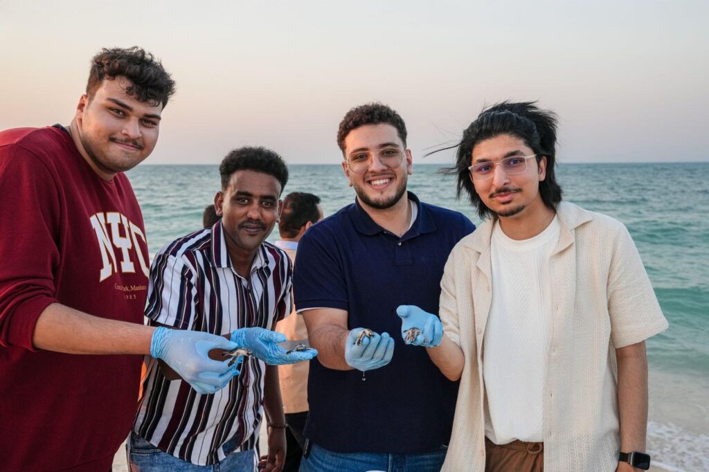 Barzan University College students carefully hold rescued Hawksbill sea turtle hatchlings during a conservation experience at Fuwairit Beach.